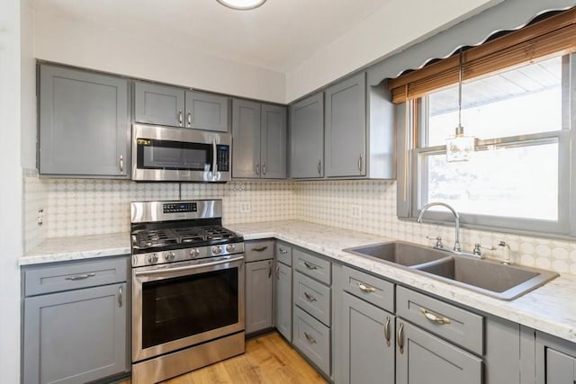 kitchen featuring a sink, stainless steel appliances, gray cabinetry, and decorative backsplash