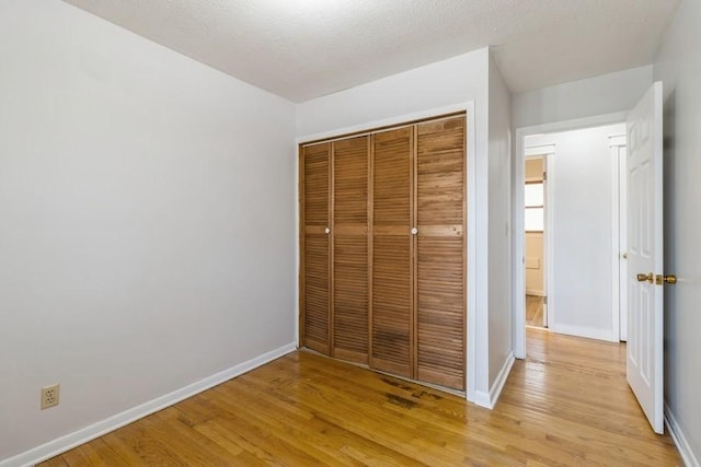 unfurnished bedroom with a closet, baseboards, light wood-style floors, and a textured ceiling