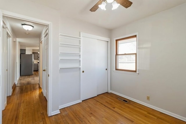 unfurnished bedroom with visible vents, baseboards, freestanding refrigerator, wood finished floors, and a closet