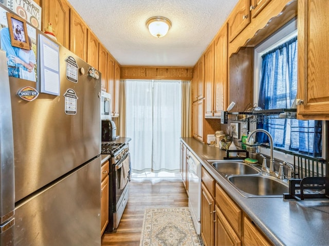 kitchen featuring range with gas cooktop, dishwasher, light wood-style flooring, freestanding refrigerator, and a sink