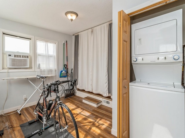 washroom featuring cooling unit, wood finished floors, baseboards, stacked washing maching and dryer, and laundry area