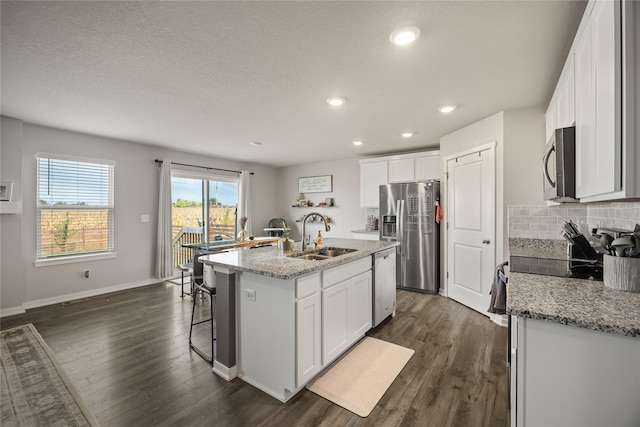 kitchen with a sink, backsplash, dark wood finished floors, stainless steel appliances, and a kitchen island with sink