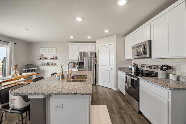 kitchen with backsplash, appliances with stainless steel finishes, dark wood-style floors, white cabinets, and a sink