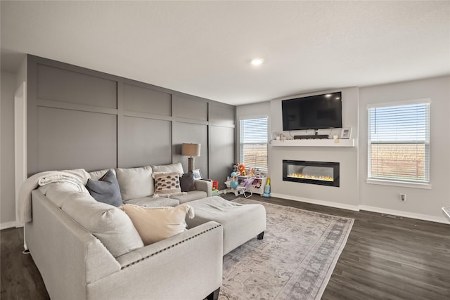 living area featuring a glass covered fireplace, a decorative wall, dark wood finished floors, and baseboards