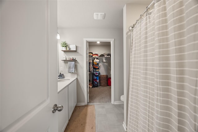 bathroom featuring a walk in closet, toilet, curtained shower, baseboards, and vanity