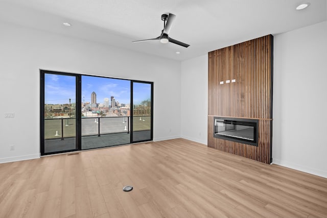 unfurnished living room with a glass covered fireplace, a view of city, wood finished floors, and a ceiling fan