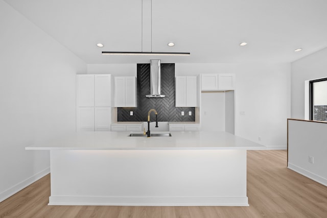 kitchen with an island with sink, a sink, tasteful backsplash, white cabinetry, and wall chimney exhaust hood