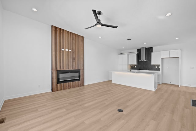 unfurnished living room with a glass covered fireplace, visible vents, light wood finished floors, and ceiling fan