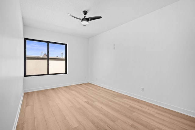 empty room featuring a ceiling fan, baseboards, and light wood finished floors