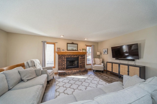 living room with a brick fireplace, a textured ceiling, and wood finished floors