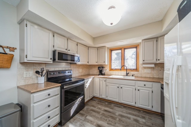 kitchen featuring wood finished floors, a sink, decorative backsplash, light countertops, and appliances with stainless steel finishes