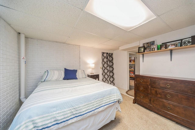 bedroom with a paneled ceiling, light carpet, and brick wall