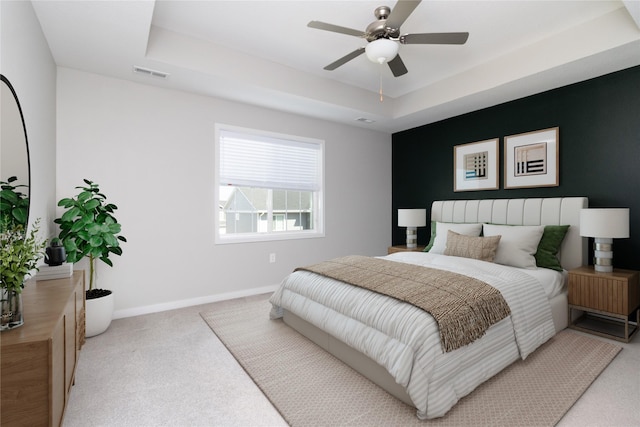 carpeted bedroom with baseboards, a raised ceiling, visible vents, and a ceiling fan