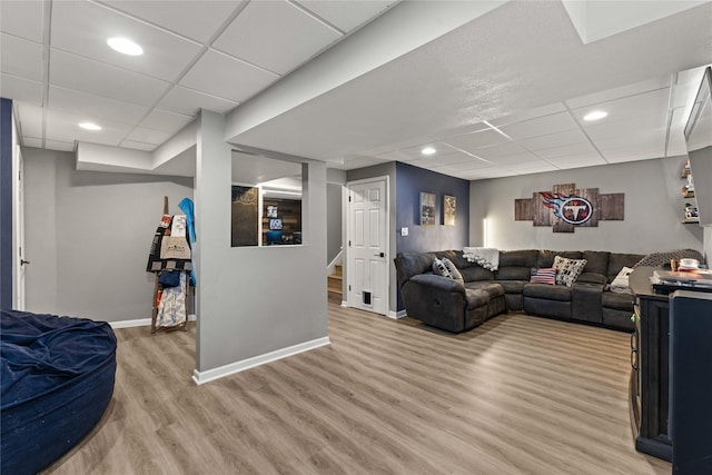 living area with light wood finished floors, a drop ceiling, stairway, and baseboards