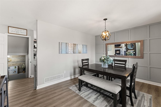 dining room featuring baseboards, visible vents, dark wood finished floors, a decorative wall, and a chandelier