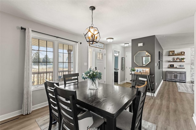 dining space featuring light wood-type flooring, visible vents, baseboards, and a chandelier