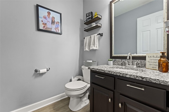 half bathroom featuring toilet, vanity, baseboards, and wood finished floors