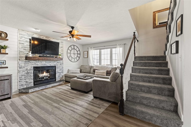 living area with wooden walls, ceiling fan, stairs, wood finished floors, and a textured ceiling