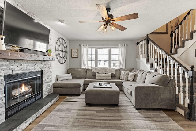 living area featuring stairway, a fireplace, wood finished floors, a textured ceiling, and a ceiling fan