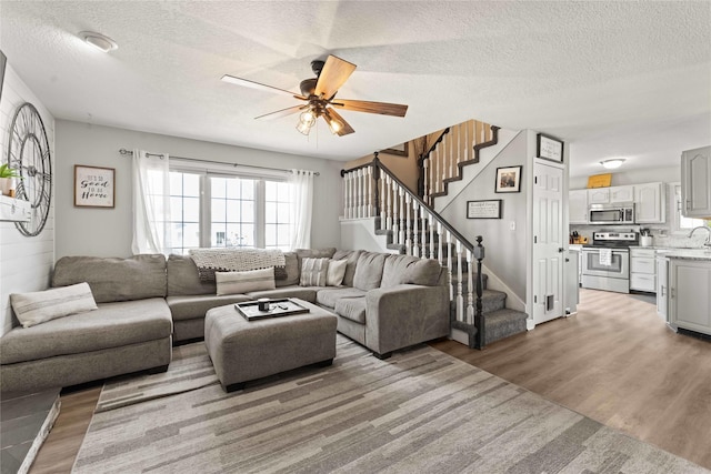 living area with light wood finished floors, stairway, a textured ceiling, and ceiling fan