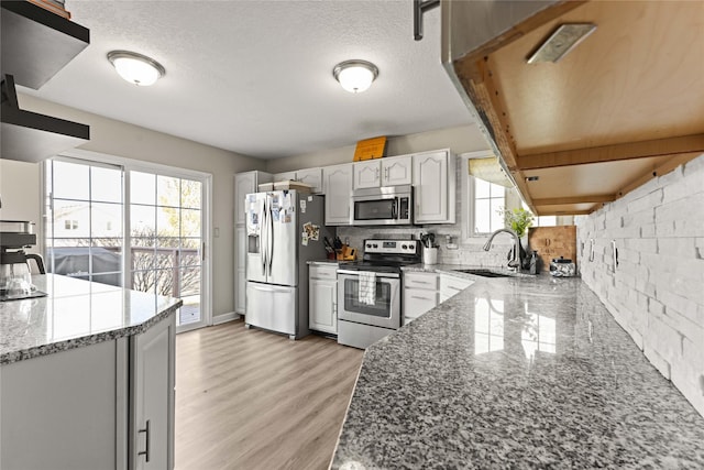 kitchen with light stone countertops, a sink, stainless steel appliances, tasteful backsplash, and light wood-type flooring