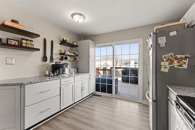 kitchen featuring open shelves, light wood-type flooring, light stone counters, and freestanding refrigerator