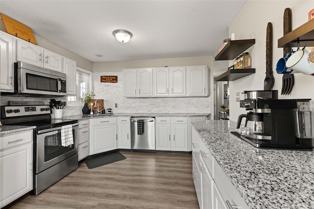 kitchen with white cabinets, appliances with stainless steel finishes, light wood-type flooring, and light stone countertops