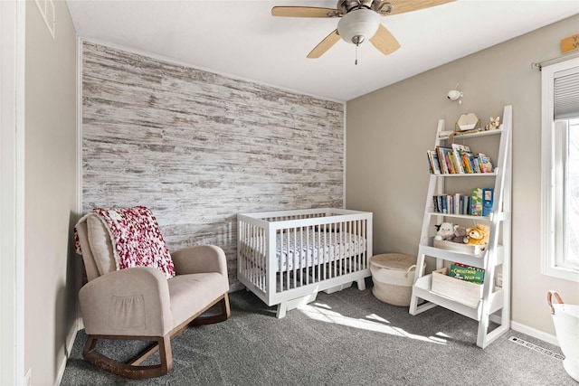 carpeted bedroom with an accent wall, a crib, baseboards, and ceiling fan