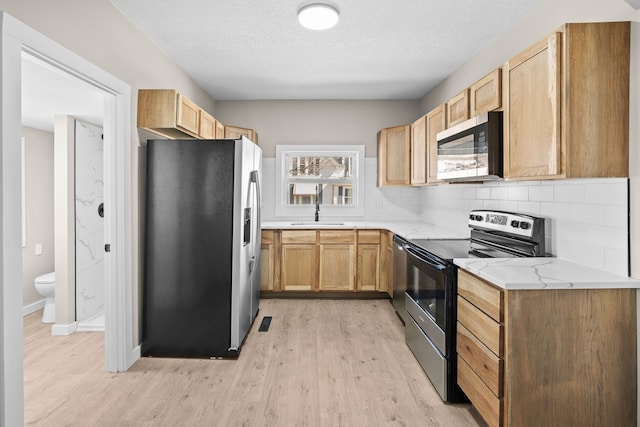 kitchen with backsplash, light stone countertops, light wood-style flooring, stainless steel appliances, and a textured ceiling