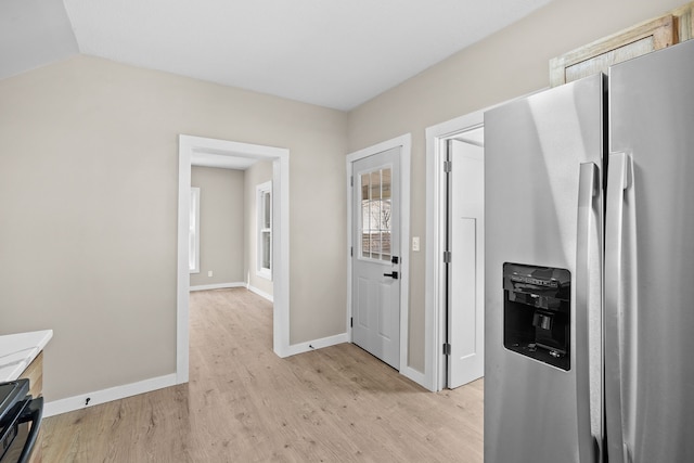 kitchen with light wood-style flooring, stainless steel fridge, baseboards, stove, and vaulted ceiling