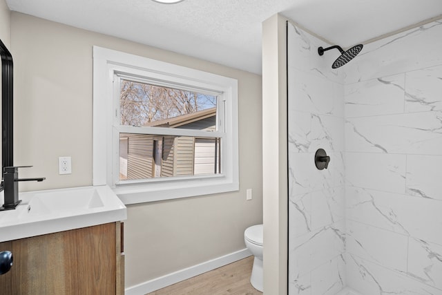 bathroom with baseboards, toilet, tiled shower, wood finished floors, and vanity