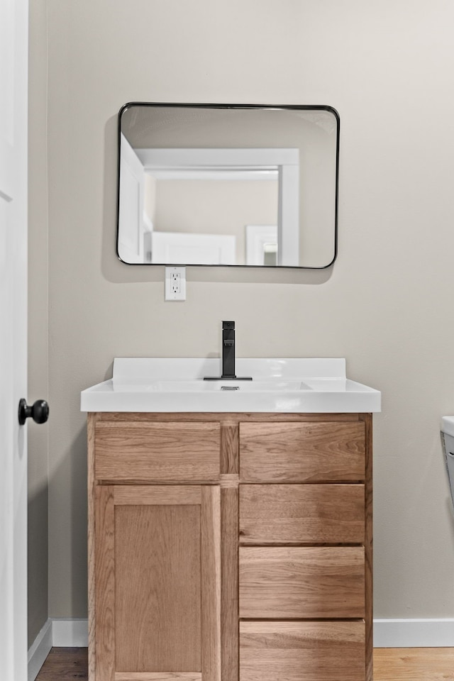 half bathroom featuring toilet, vanity, baseboards, and wood finished floors