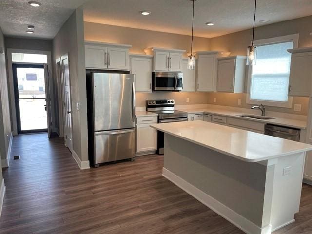 kitchen featuring dark wood-type flooring, a center island, appliances with stainless steel finishes, and a sink