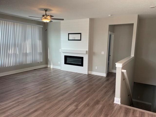 unfurnished living room featuring a large fireplace, baseboards, dark wood-type flooring, and ceiling fan