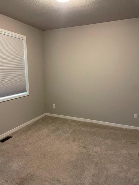 empty room with visible vents, carpet floors, a textured ceiling, and baseboards