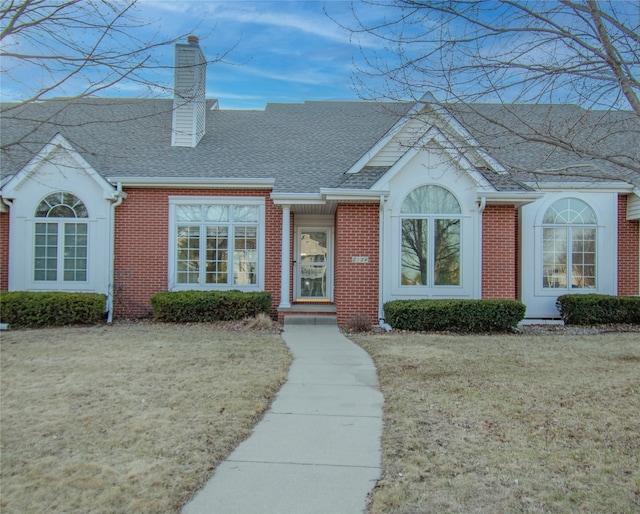 view of front of property featuring a front yard, brick siding, roof with shingles, and a chimney