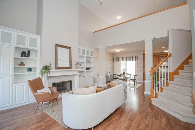 living area featuring stairway, wood finished floors, decorative columns, a tile fireplace, and a towering ceiling