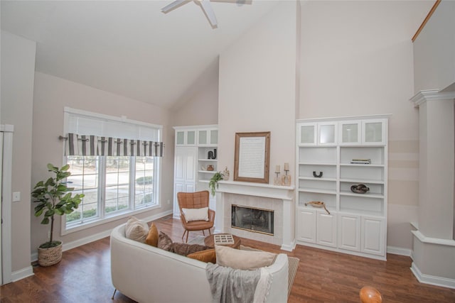 living area featuring baseboards, ceiling fan, a tiled fireplace, dark wood-style floors, and high vaulted ceiling