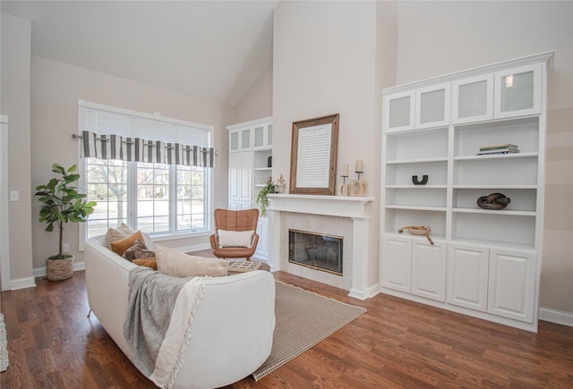 living area featuring high vaulted ceiling, baseboards, dark wood-type flooring, and a tiled fireplace