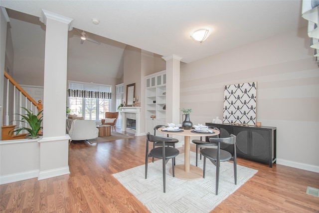 dining area featuring baseboards, stairway, lofted ceiling, light wood-style floors, and ornate columns