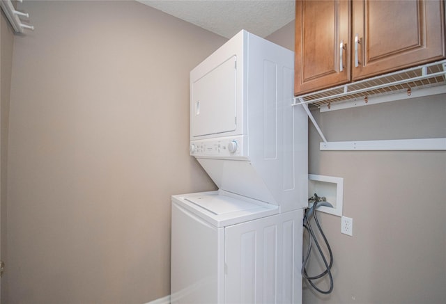 laundry room featuring cabinet space, a textured ceiling, and stacked washer / dryer