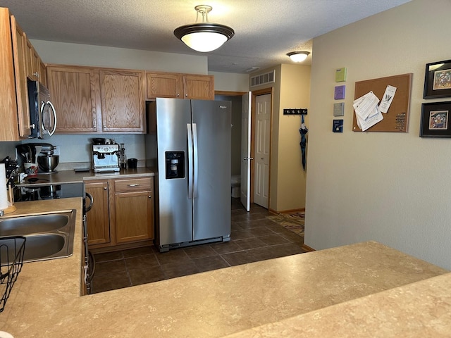 kitchen featuring visible vents, dark tile patterned flooring, a sink, stainless steel appliances, and light countertops