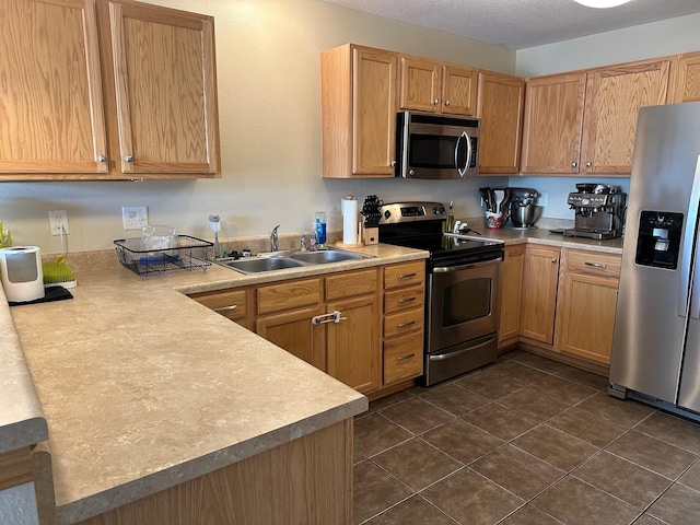 kitchen with dark tile patterned floors, a sink, a textured ceiling, appliances with stainless steel finishes, and light countertops