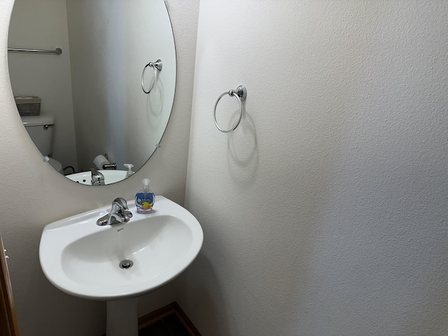 bathroom featuring toilet, a textured wall, and a sink