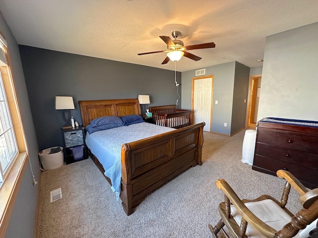 bedroom featuring a ceiling fan, light colored carpet, visible vents, and a textured ceiling