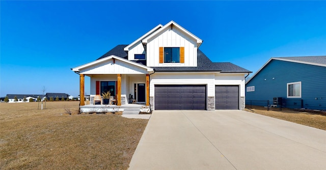 modern inspired farmhouse featuring board and batten siding, a front yard, covered porch, stone siding, and driveway