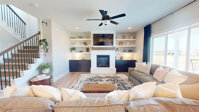 living area featuring visible vents, ceiling fan, stairs, wood finished floors, and a glass covered fireplace