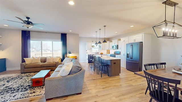 living area with recessed lighting, light wood-type flooring, baseboards, and ceiling fan with notable chandelier