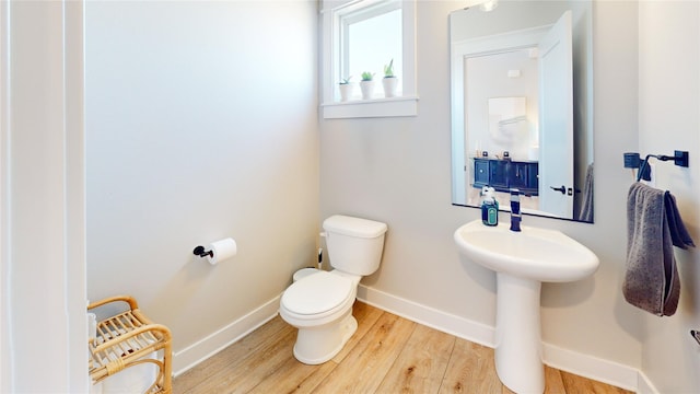 half bathroom with toilet, wood finished floors, baseboards, and a sink