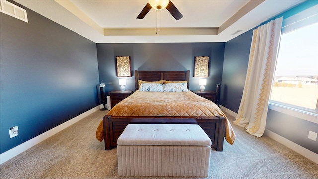 bedroom with a tray ceiling, visible vents, and baseboards